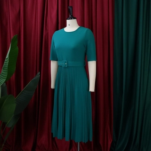Detail of dark green pleated dress featuring a crew neck and waist belt on a mannequin