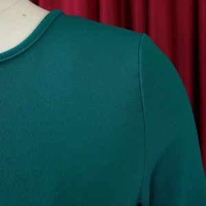 Close-up of dark green crepe fabric dress with round neck stitching and texture details