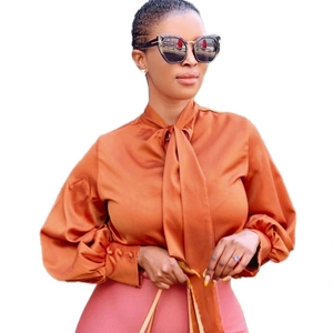 Details einer eleganten Satinbluse in Karamell mit Schleife am Hals und Laternenärmeln
