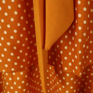 Detail of orange polka dot dress featuring ruffled edges and fabric waist tie