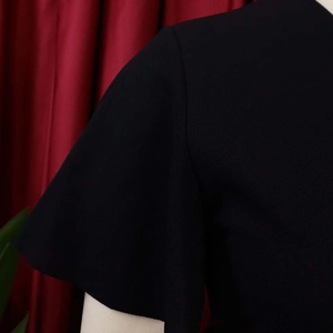 Close-up of black V-neck dress fabric texture showing shoulder seam and pleated ruffle sleeve