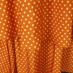 Detailed view of orange dress fabric with white polka dots and tiered ruffle hemline