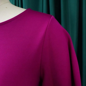 Detailed close-up of crew neck and shoulder stitching on a rose red professional dress