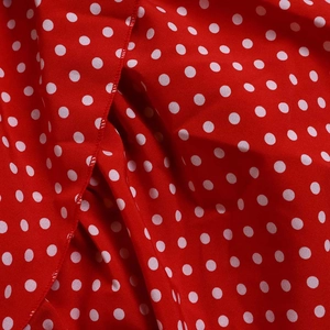 Close-up of lightweight red fabric featuring white polka dot pattern and fine stitching