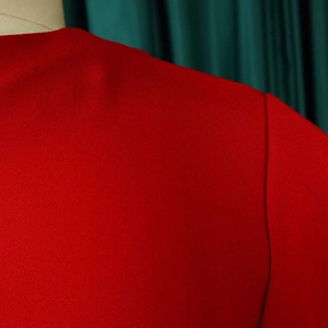 Detailed close-up of red knit fabric texture and shoulder seam stitching on dress