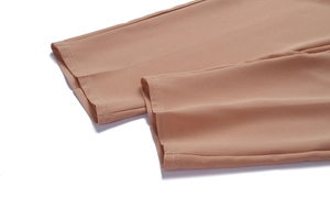 Detailed macro view of the double-stitched hem on women's light brown tailored trousers