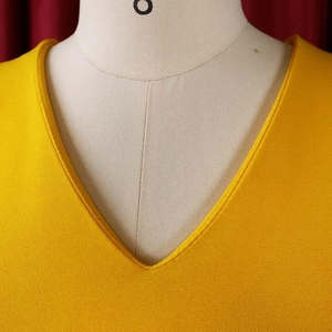 Detail of V-neckline and textured crepe fabric on a ginger yellow ruffled dress