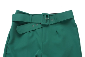 Detail of emerald green trousers featuring a wide belt with square fabric buckle and eyelets