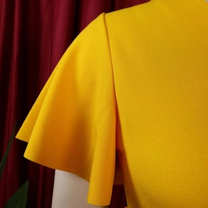 Detail of yellow V-neck dress featuring layered flutter sleeves and textured crepe fabric