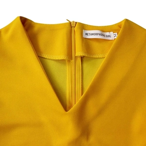 Detail view of V-neckline and invisible back zipper on yellow pleated chiffon dress
