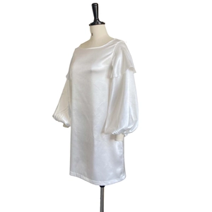 Detailed view of white satin dress featuring oversized puff sleeves and ruffled shoulders