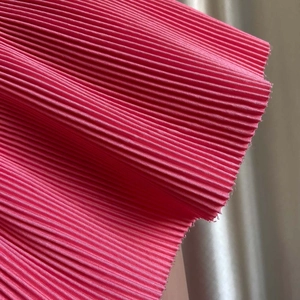 Détail macro du tissu plissé rose pêche avec des textures verticales fines en polyester