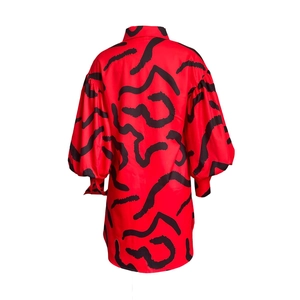 Detail view of bright red maxi shirt dress featuring black abstract wave patterns and lantern sleeves