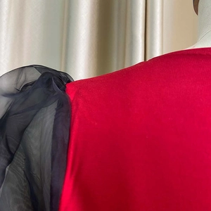Detail of red knit dress with black sheer mesh puff sleeves and refined shoulder stitching