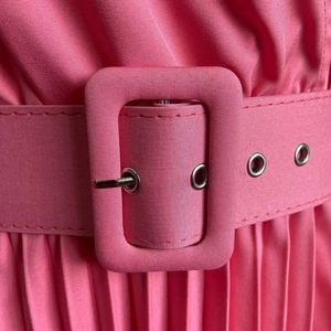 Détail de robe plissée rose avec ceinture large, boucle rectangulaire et œillets métalliques