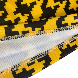 Detailed close-up of yellow and black pixelated print fabric with white overlock stitching