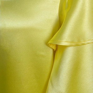 Detail of yellow satin fabric featuring soft ruffles and elegant glossy finish