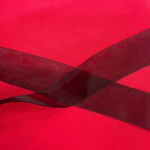 Close-up of red twill fabric texture with elegant sheer burgundy organza ribbon detail