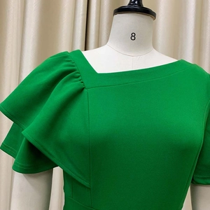 Detailed view of grass green dress with asymmetric neckline and layered ruffle sleeves