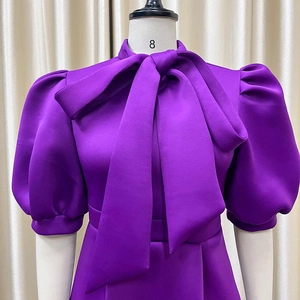 Detail of elegant purple satin party dress featuring a large bow neckline and puff sleeves