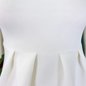 Detailed close-up of pleated waist design on white dress featuring double layer ruffles