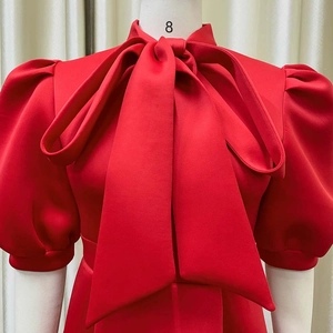 Detail view of red cocktail dress featuring oversized bow neckline and puff sleeves