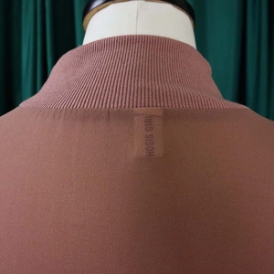 Detail van de terracotta chiffon jurk met geribbelde halslijn en een merklabel in de nek