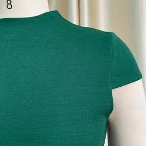 Détail du tissu texturé vert foncé montrant le col montant et les manches courtes