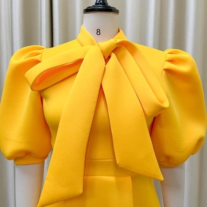 Detail of elegant yellow dress featuring oversized bow neckline and vintage puff sleeves