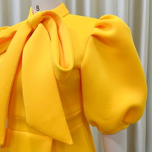Detail of bright yellow dress featuring elegant oversized bow tie and puff sleeves