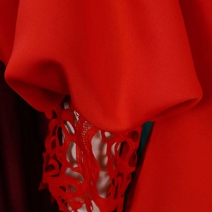 Detailed close-up of vibrant red fabric with ruffle sleeves and intricate lace stitching