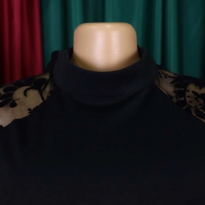 Detail of high neck black jumpsuit with sheer mesh lantern sleeves and floral lace texture