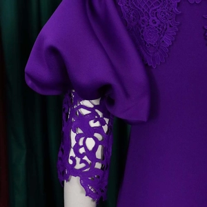 Detail of purple dress featuring lace flower appliques and puff sleeves on velvet background