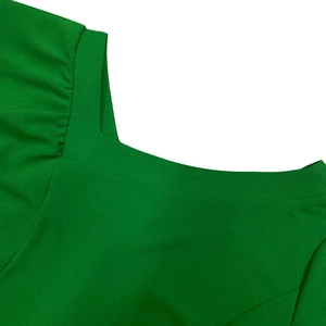 Detail of emerald green dress featuring a square neckline and fine pleated shoulder texture