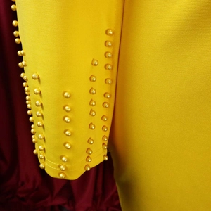 Détail macro d'une manche jaune vif ornée de rangées de perles dorées métallisées