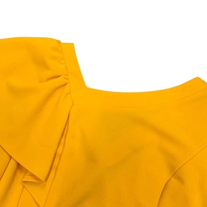 Detailed view of yellow ruffled asymmetric neckline and pleated stitching on elegant dress