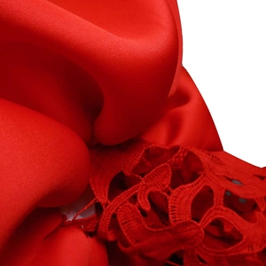 Close-up of red satin fabric with detailed floral lace embroidery on an off-shoulder dress