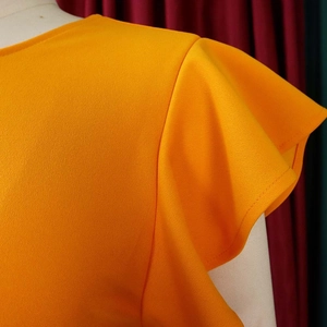 Detail of vibrant orange dress showing round neckline and ruffled cap sleeve textures