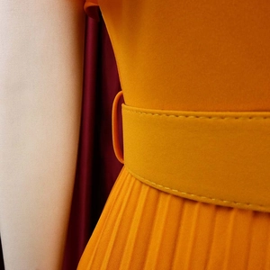 Detailed view of bright orange pleated dress with matching belt and fine stitching work