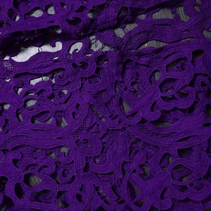 Close-up of deep purple lace fabric with intricate floral embroidery and textured patterns