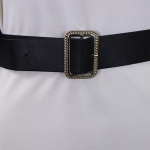 Detail of a black leather belt with a textured gold rectangular buckle on a white dress