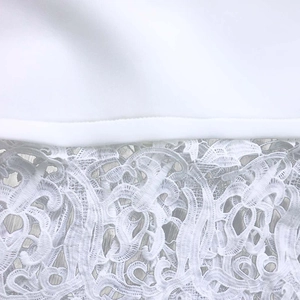Close-up of white dress showing elegant lace patchwork and floral hollow-out embroidery detail