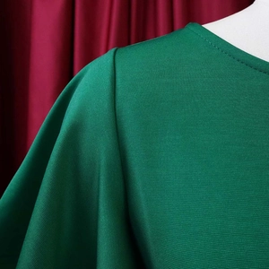 Close-up of emerald green knit dress showing ruffled shoulder pleats and collar detail