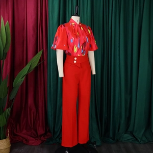 Detail der roten Blumenbluse mit Schleife und Hose mit goldenen Zierknöpfen