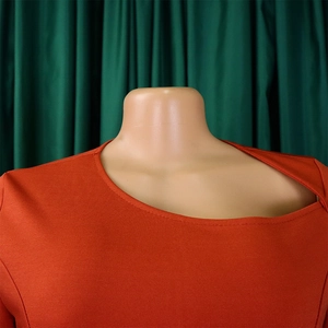 Detail of bright orange dress with asymmetrical cutout neckline on a mannequin