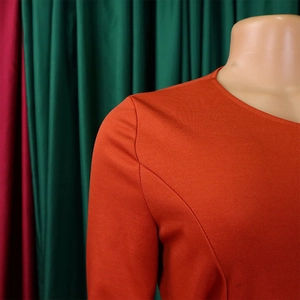 Macro detail of the orange knit fabric texture and high-quality stitching on a round neck dress