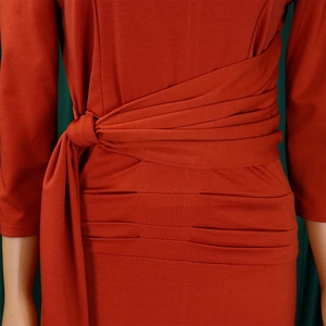 Detail of waist design with side tie knot and elegant pleats on a red midi dress