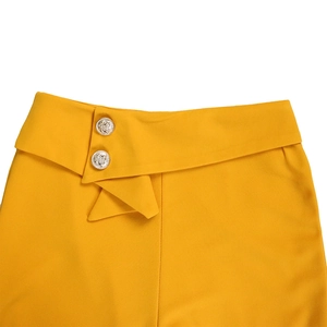 Detailansicht der senfgelben High-Waist-Shorts mit geprägten Löwenkopf-Metallknöpfen
