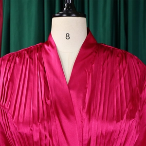 Detail der plissierten Satinstruktur und des tiefen V-Ausschnitts dieses rosa Outfits