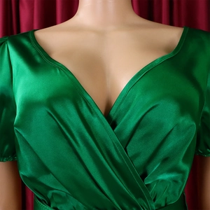 Close-up of shiny green satin fabric and V-neck pleated detail on women's dress